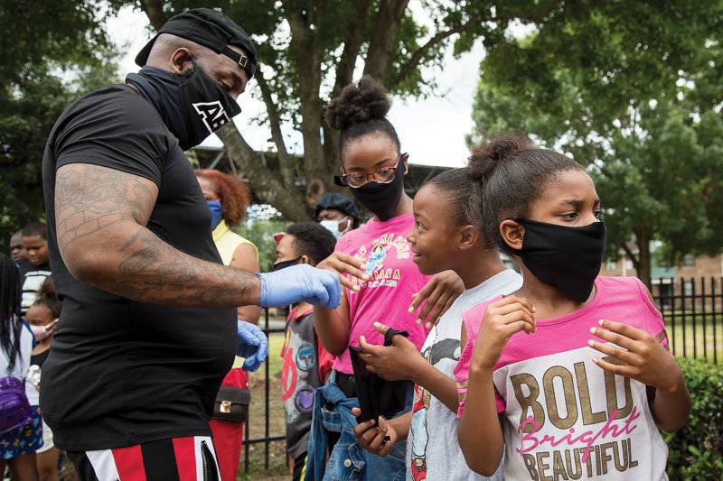 The Houston Chronicle’s “One Year Later” visual project depicted residents “then” and “now” during the COVID-19 pandemic. Seen here is rap artist Trae Tha Truth and his Relief Gang hand out masks to kids in Third Ward on May 13, 2020.